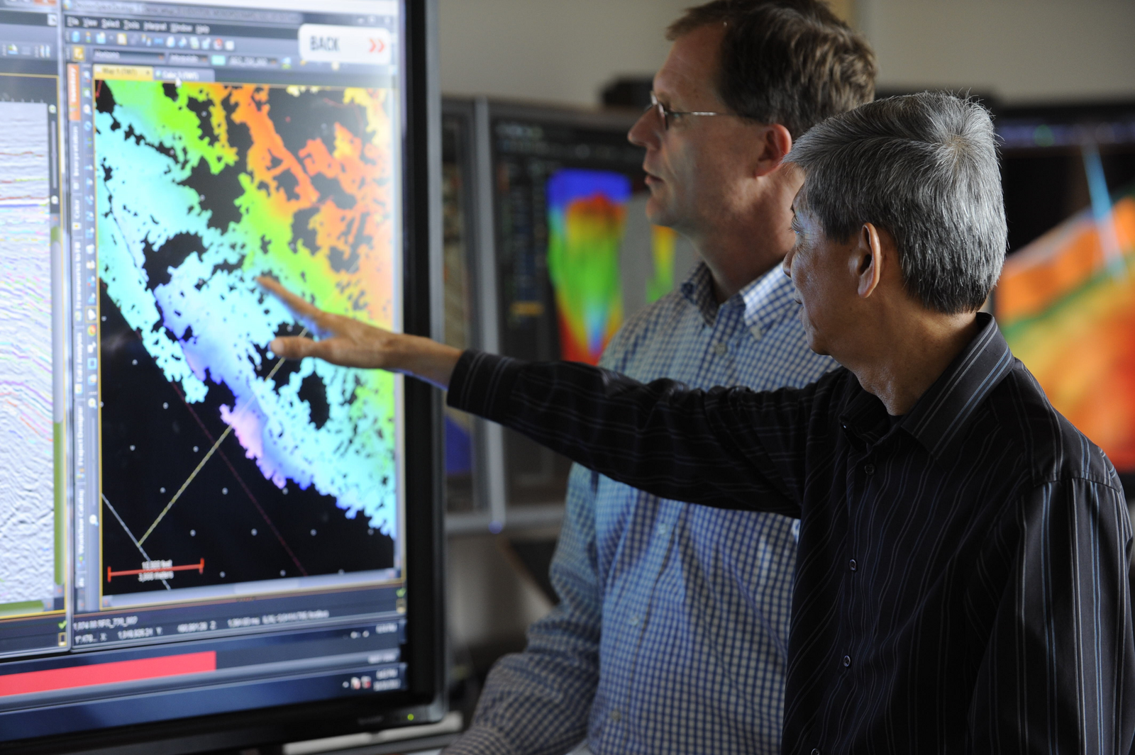 Two experts analyzing geological data on a computer displaying a colorful seismic attribute map using Halliburton technology.